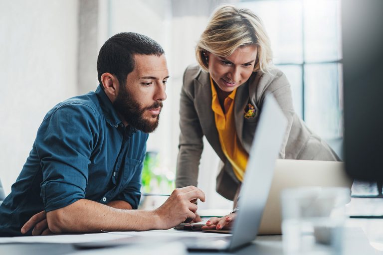 Two colleagues engaged, focused on laptop screen in an office setting