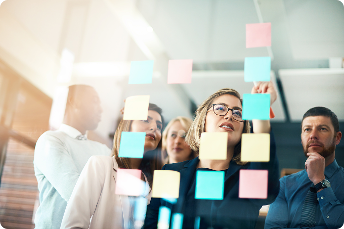 Woman organizing sticky notes on glass with focused team