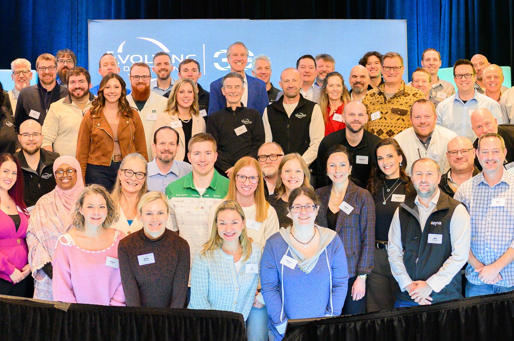 Group of people smiling at an event, standing in front of a blue banner with "Evolving Solutions" and logo