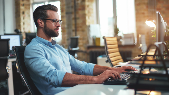 Man at desk typing on keyboard in modern office space