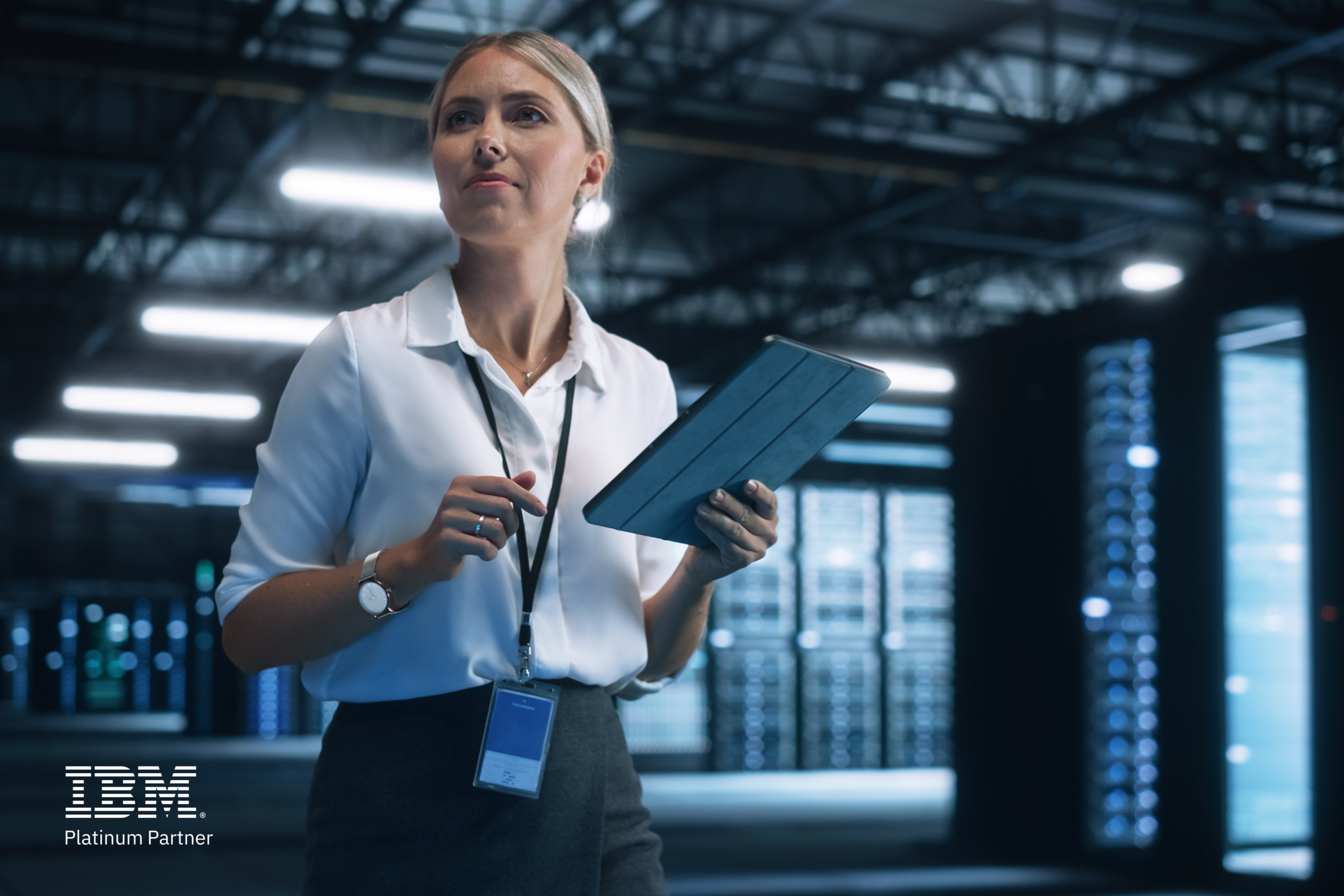 Woman in server room holding a tablet, wearing a lanyard. IBM Platinum Partner logo displayed