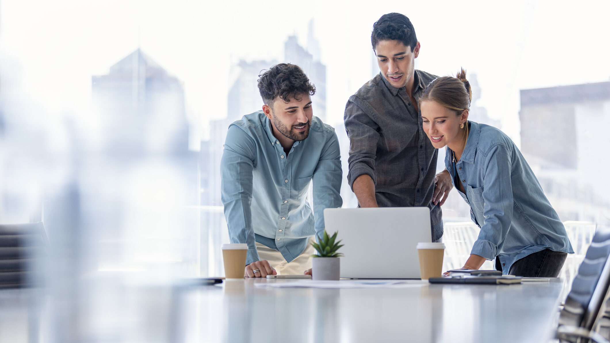 Three colleagues collaborating around a laptop in a bright office