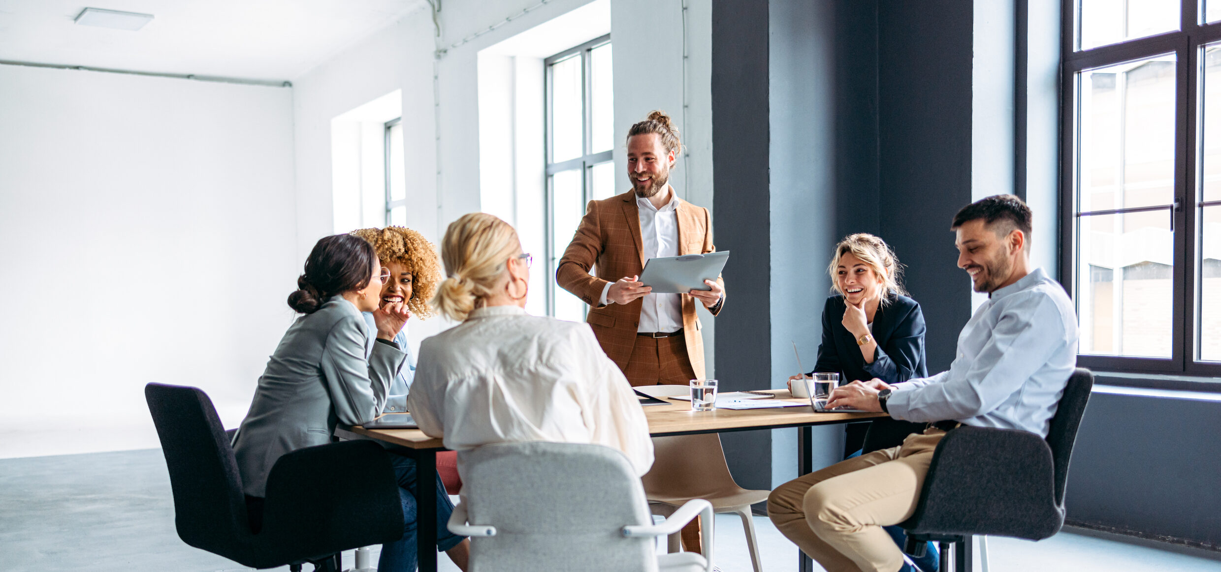 Group meeting with six people discussing around a table in a bright office