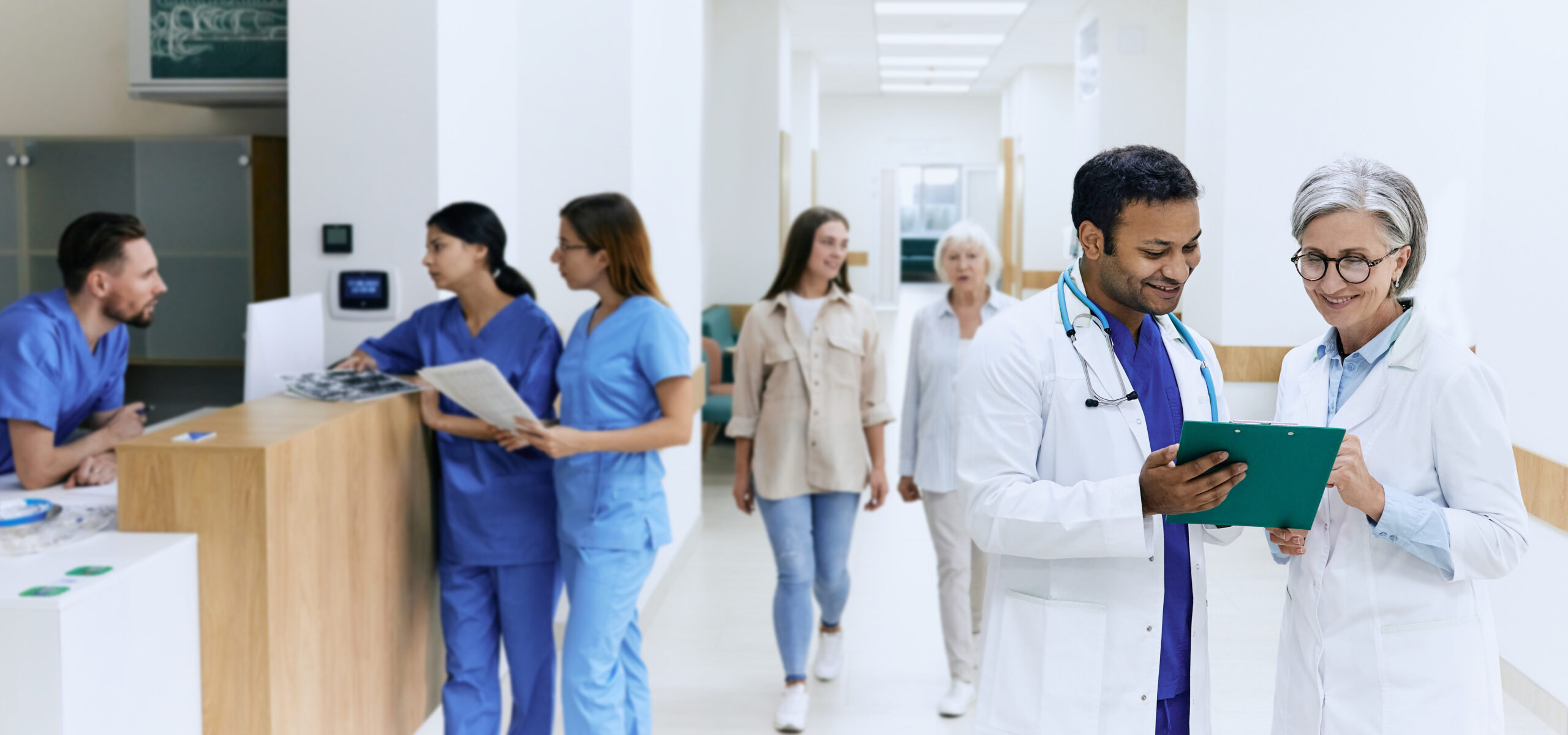 Healthcare professionals in a hospital corridor discussing patient information with colleagues and patients nearby
