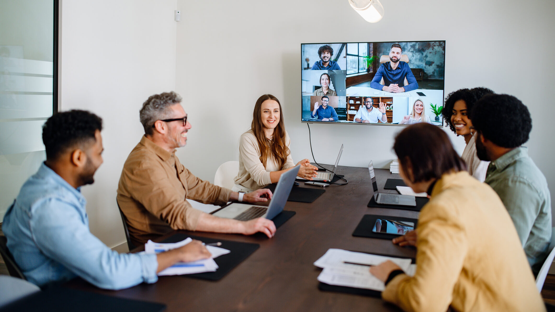 Colleagues in a conference room participating in a hybrid meeting with remote team on a video call screen