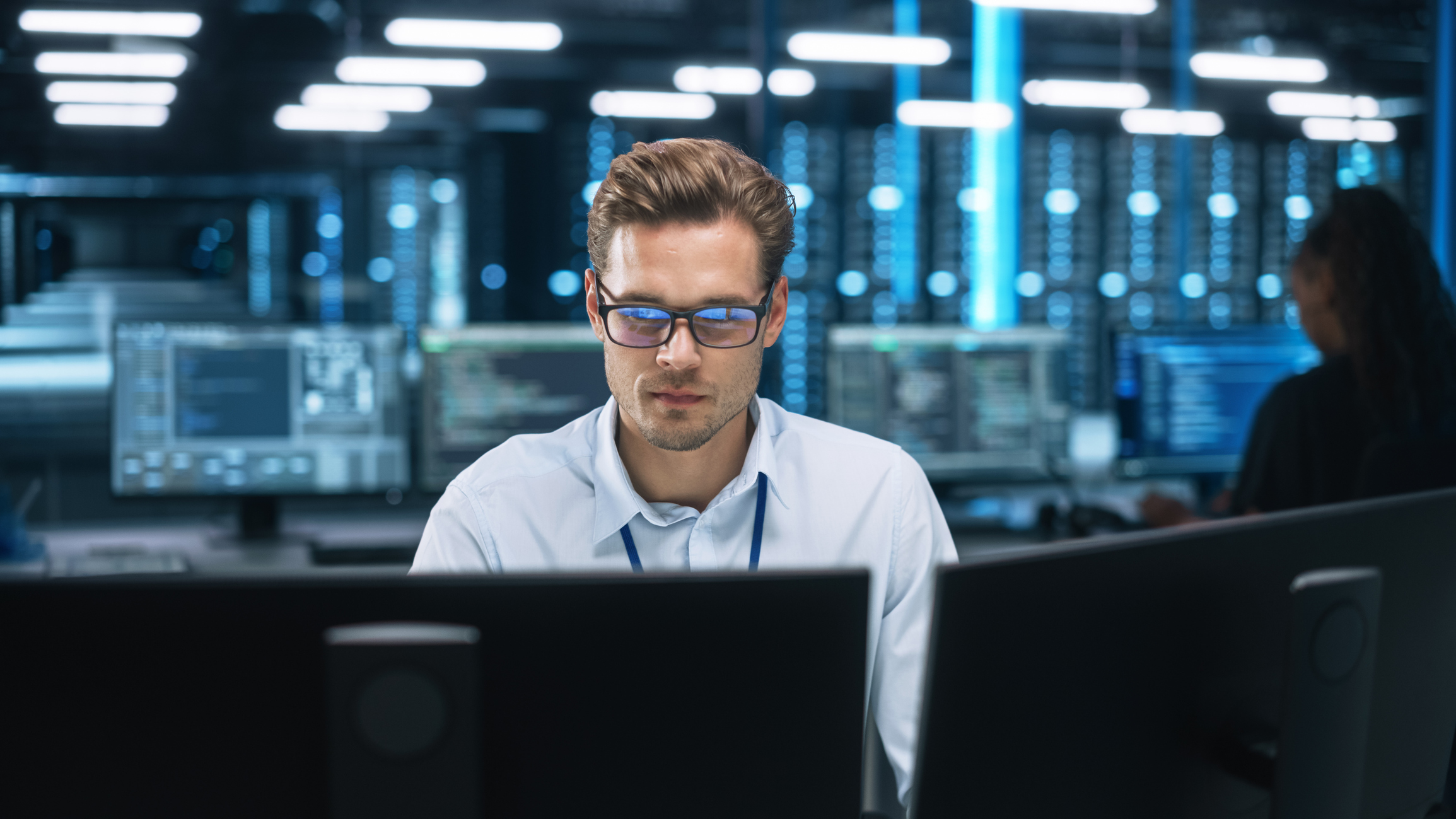 Man concentrating on multiple computer screens in a data center, surrounded by digital code
