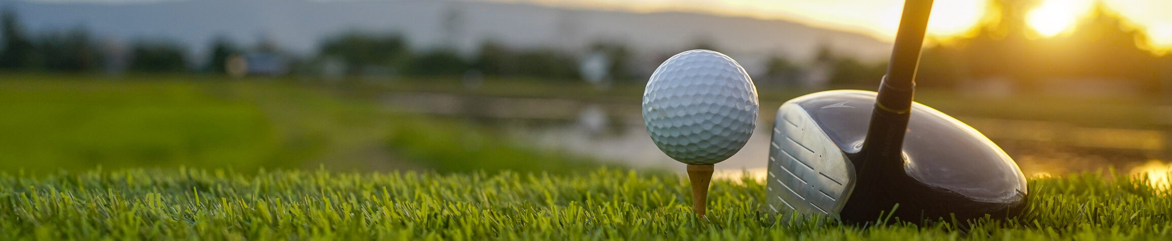 Golf ball on a tee with a driver, sunset in background
