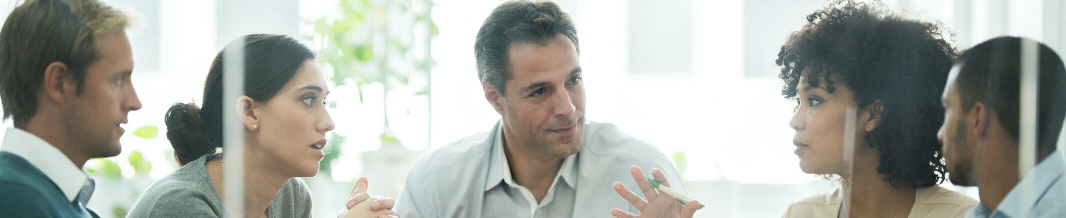 Five people in a meeting, engaged in discussion, focused expressions