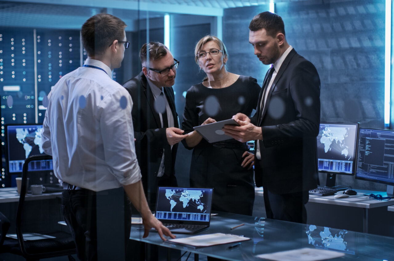 Four professionals discussing data in a technology control room